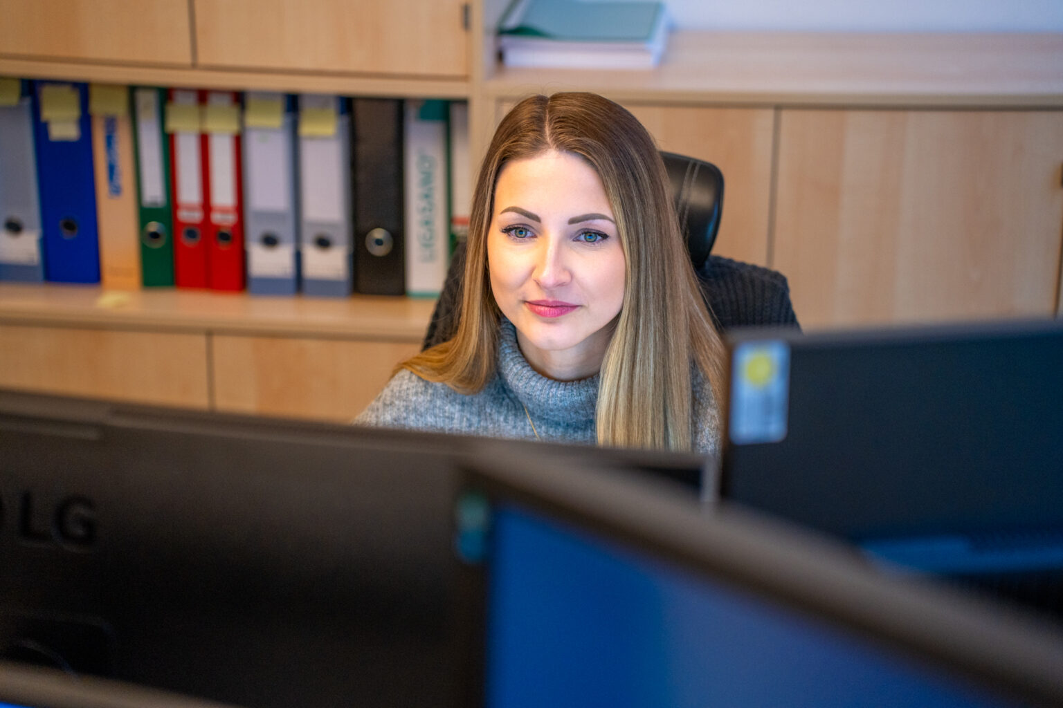 Frau arbeitet konzentriert am Computer mit Akten im Hintergrund
