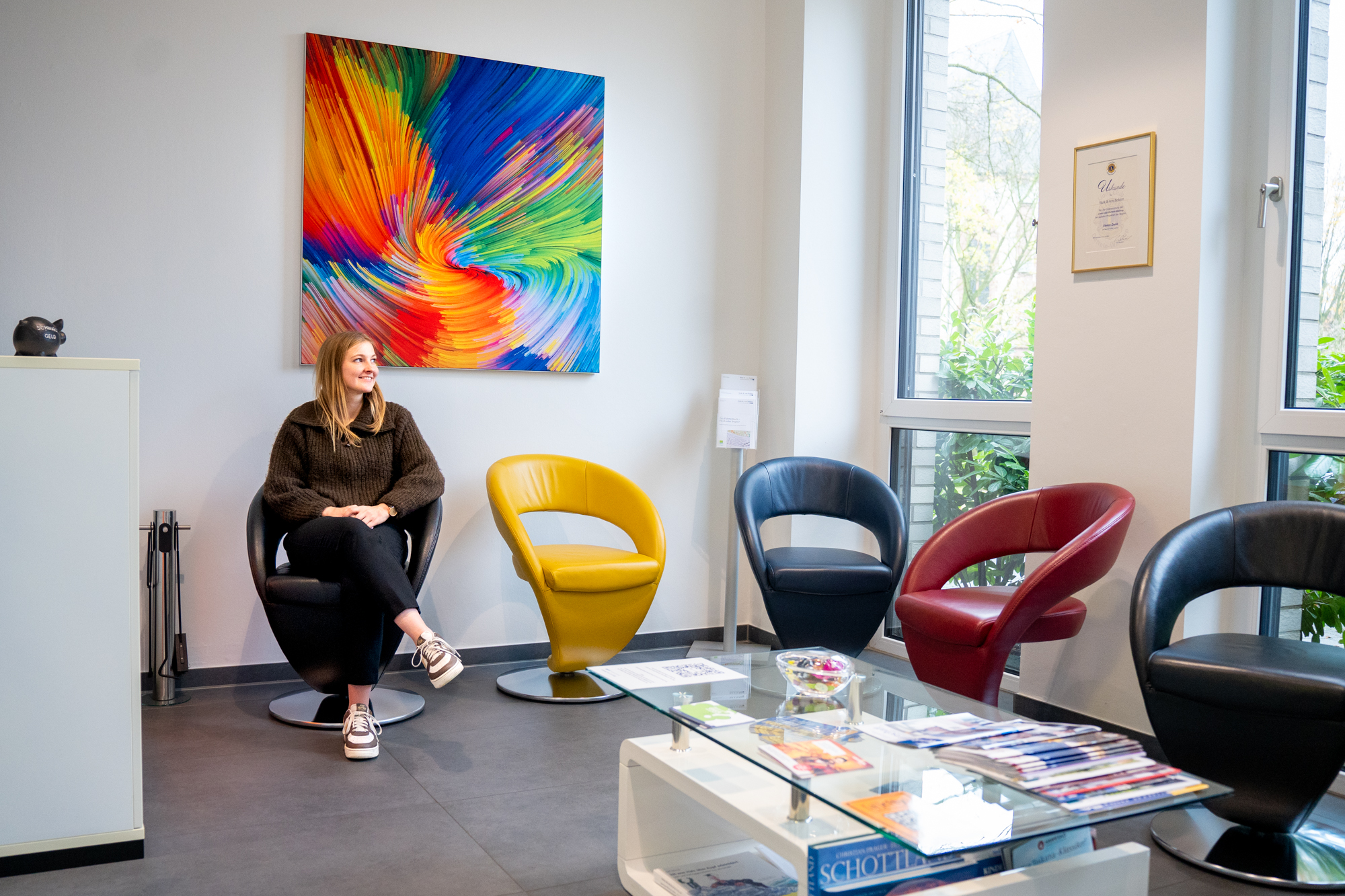 Frau sitzt im Wartebereich auf einem schwarzen Stuhl, bunte Kunst an der Wand