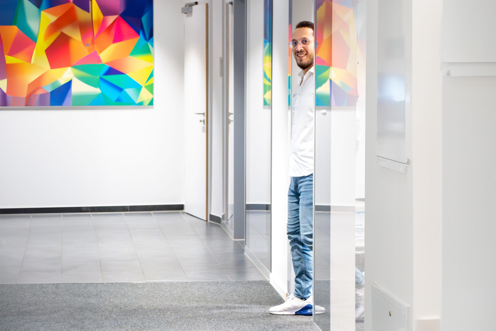 Mann steht lächelnd in einer geöffneten Glastür, farbige Bilder an der Wand